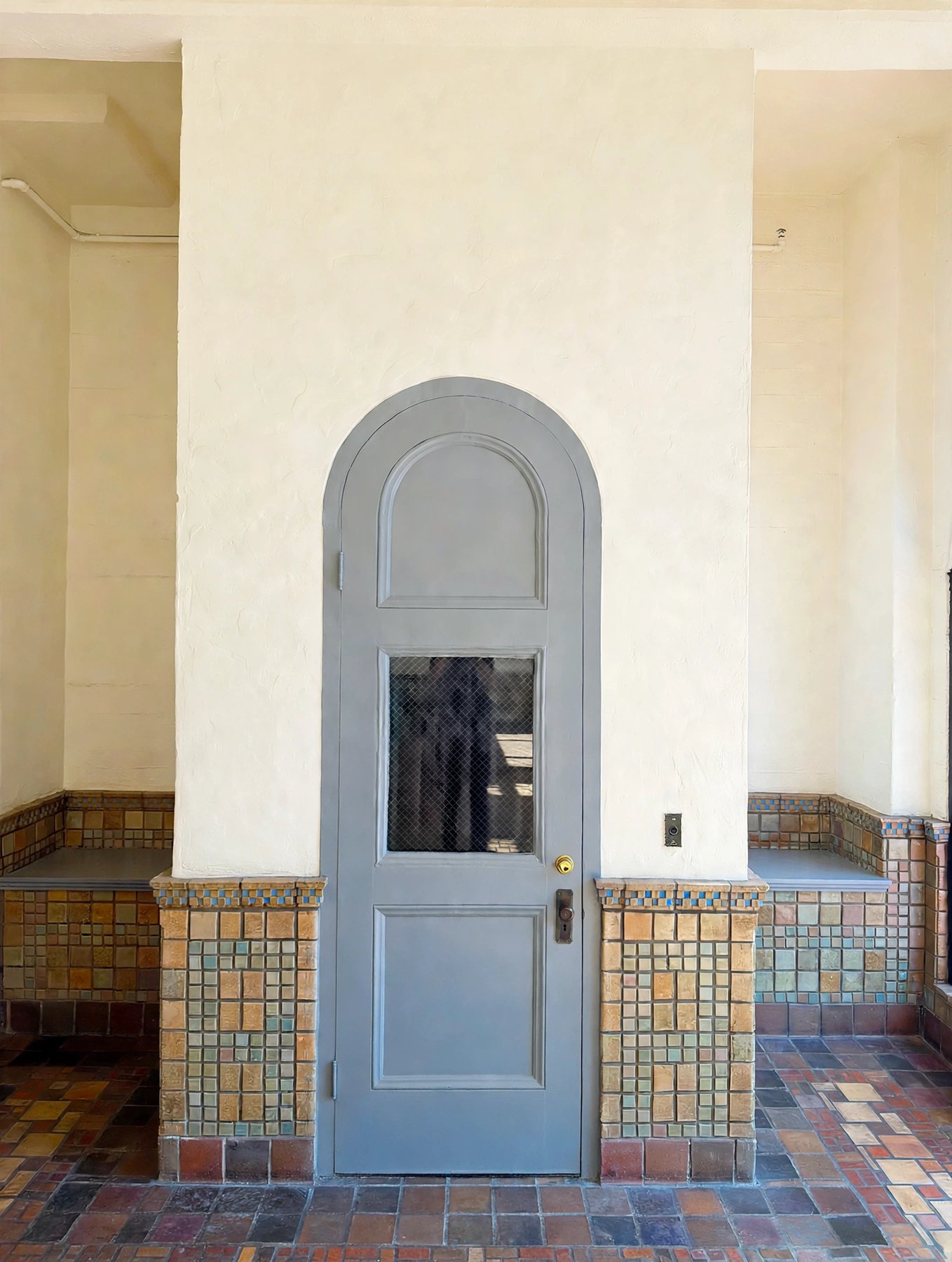 An arched door in the entrance vestibule, flanked by benches and walls faced in polychrome glazed tile above a tiled floor.
