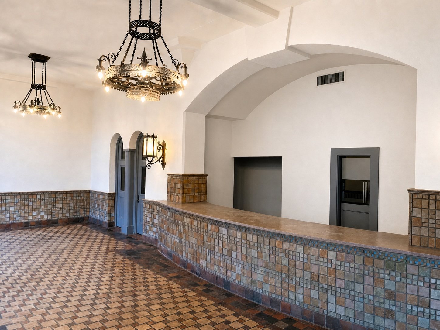 The historic lobby with a glazed-tile counter, patterned tile floor and wrought-iron chandeliers beneath a vaulted ceiling.
