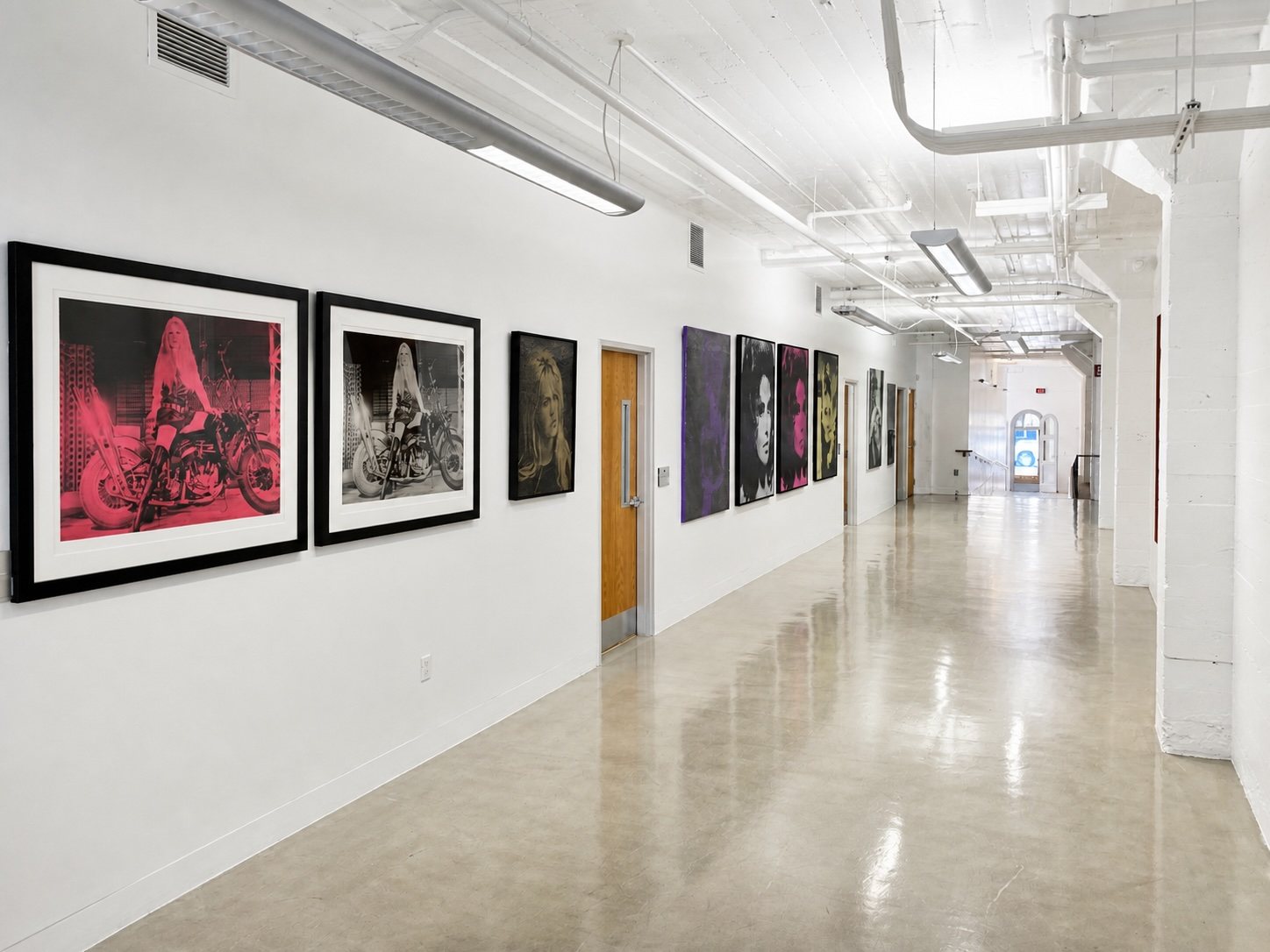 Suite 100 gallery corridor hung with framed large-format prints above a polished concrete floor.