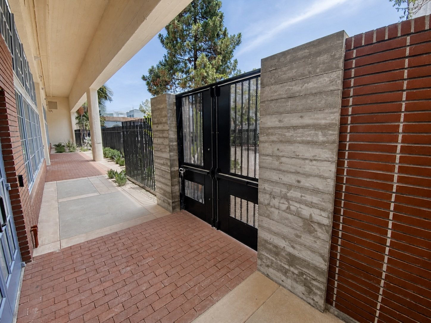Gated entrance framed by board-formed concrete and banded red brick.