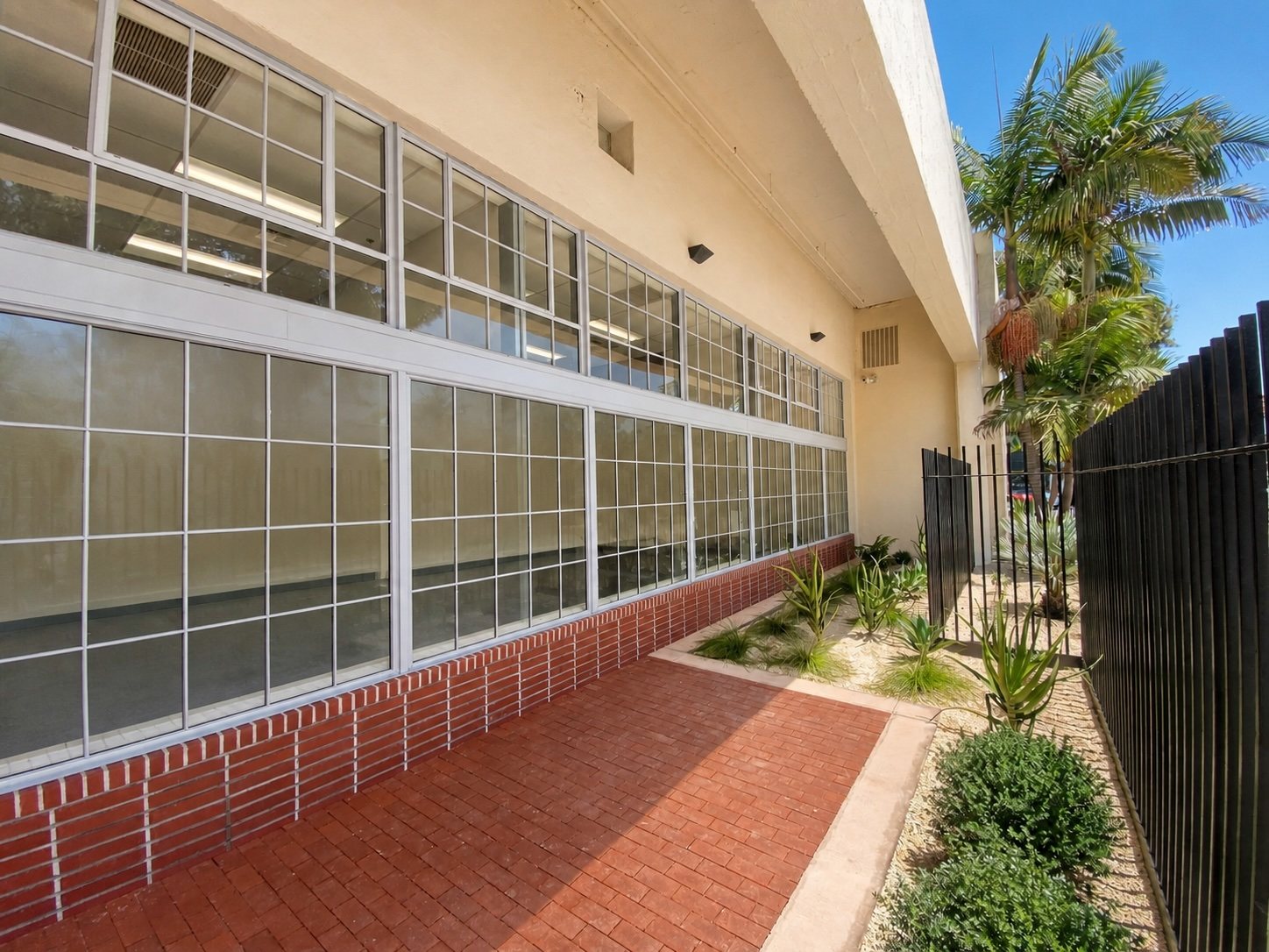 Covered walkway with brick paving running along the steel-framed window wall.