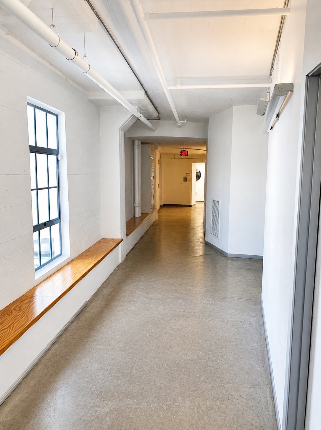 Suite 300 corridor with a continuous timber bench beneath a tall steel-framed window.