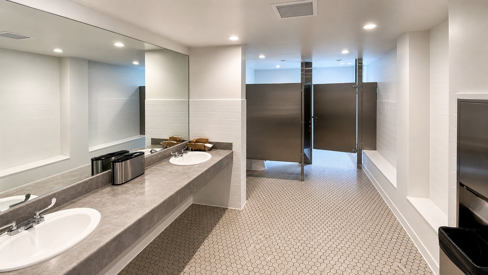 Refinished common restroom with subway tile, hex-tile floor and a stone counter.