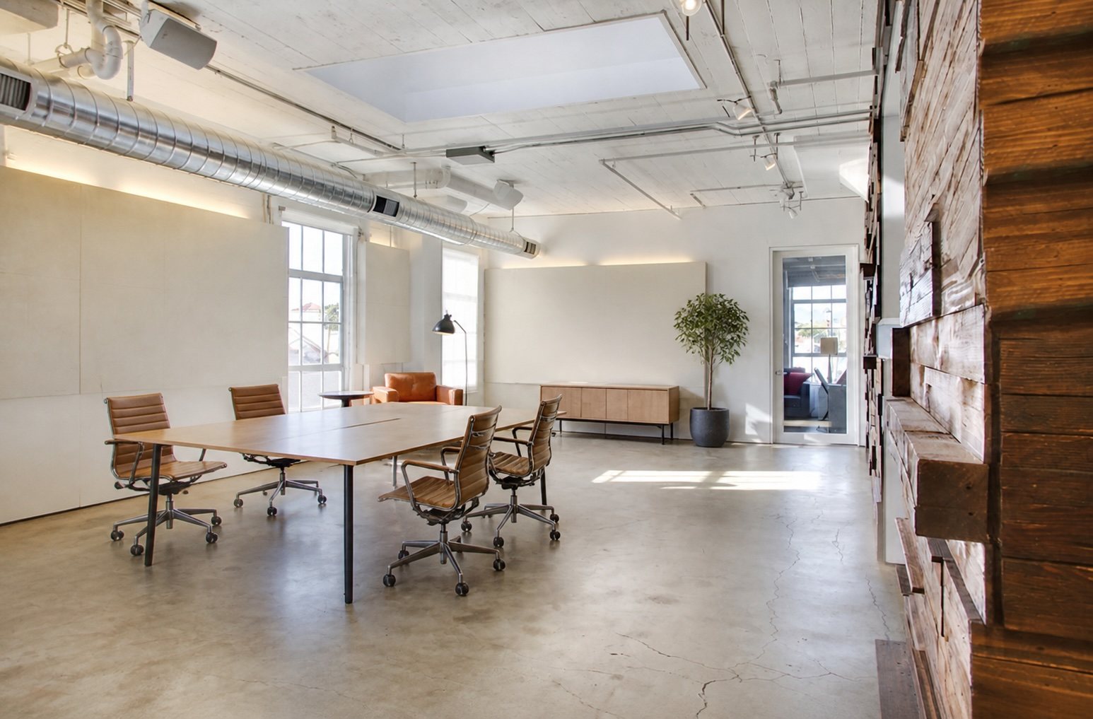 Suite 503 penthouse: an open plan beneath a skylight, with a reclaimed timber feature wall, polished concrete floor and a long meeting table.