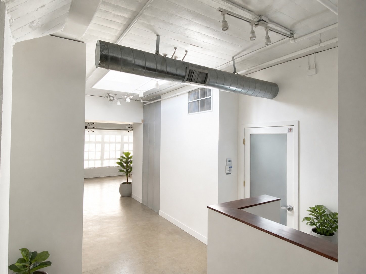Penthouse open office with standing desks, a blue sofa and daylight from a skylight and windows on two sides.